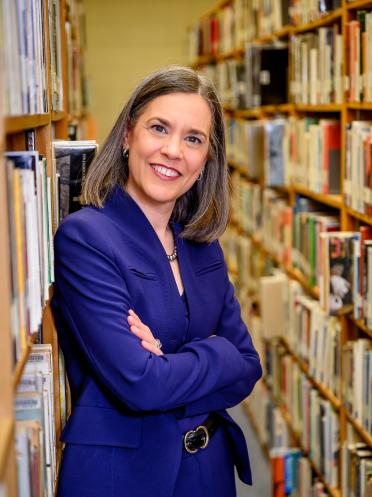 La rectrice Sophie Bouffard debout les bras croisés dans un rayon de livres de la bibliothèque.